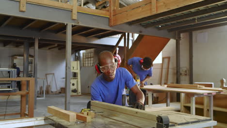 black male trainee feeding plank into table saw in workshop after instructor pointing for accuracy