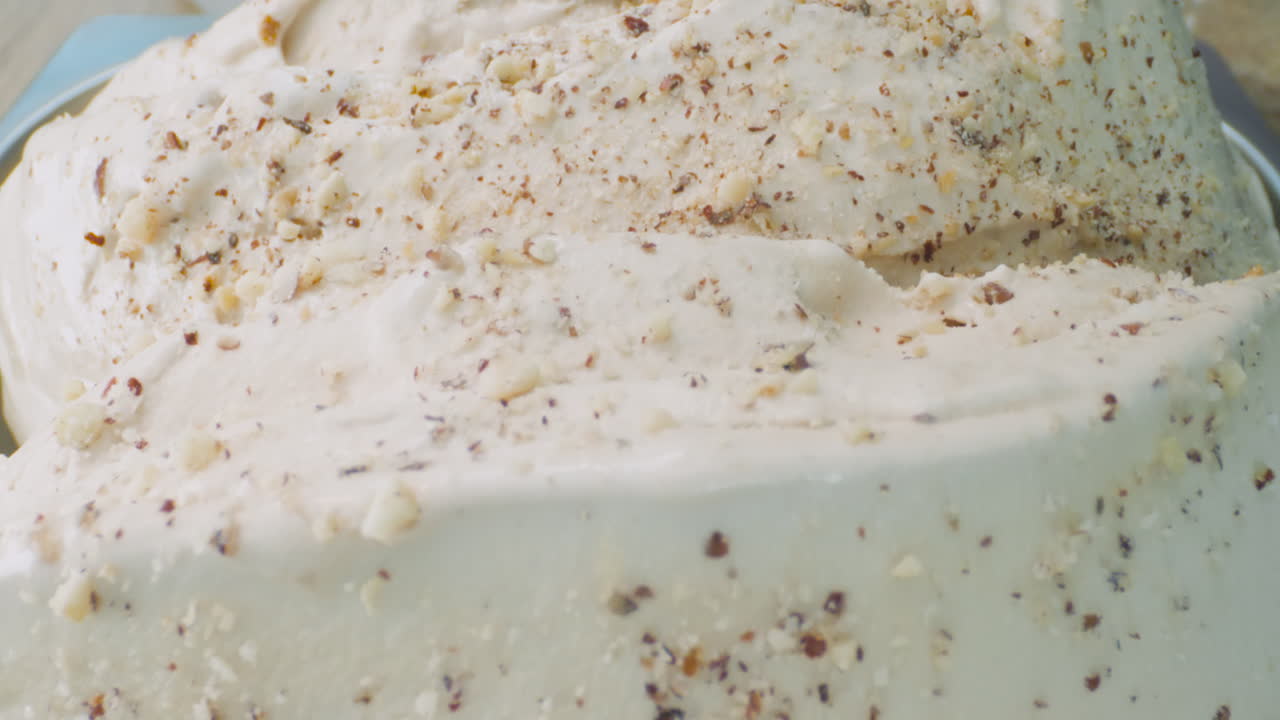 A close-up of a creamy hazelnut ice cream with hazelnut pieces falling on it. A camera shot that highlights texture, contrast, and deliciousness.