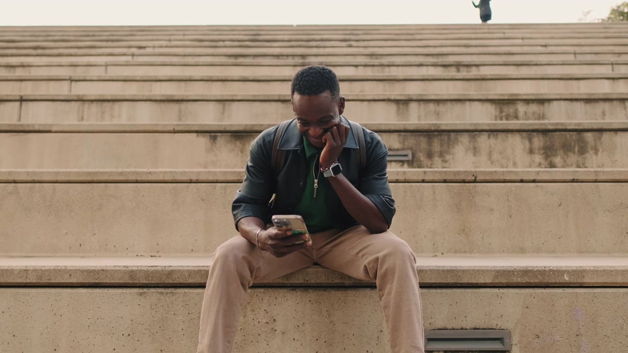Young Man Sitting on Concrete Steps Using Smartphone