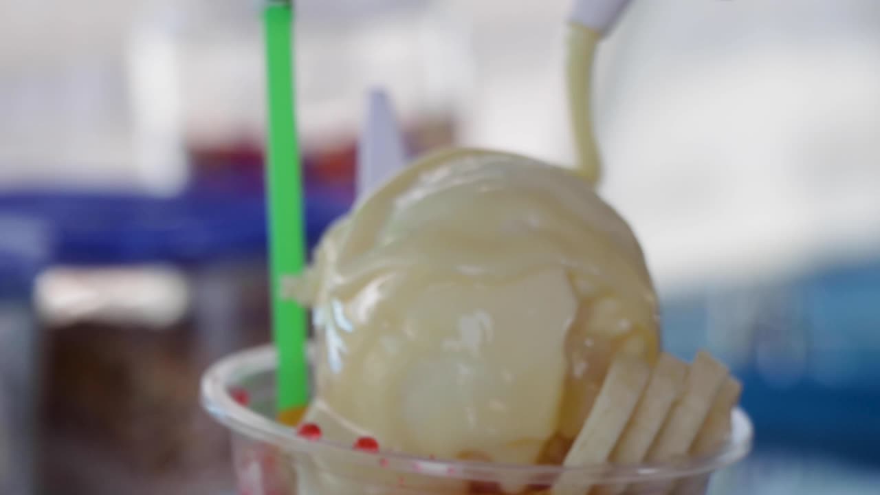 Snow cone with condensed milk being dropped in slow motion over an ice cream ball, topped with banana and fruit-flavored syrups, beach dessert, Costa Rica