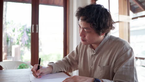 asian man writing idea plan on a notebook in a cafe