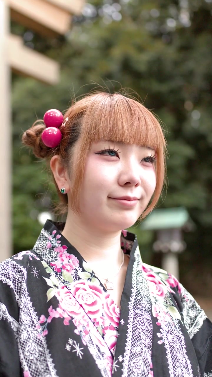 Una donna giapponese che indossa un kimono floreale tradizionale sta in piedi all'aperto vicino a un torii di un santuario shintoista