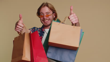 hombre turista feliz mostrando bolsas de compras, promocionando descuentos de vacaciones, asombrado por los bajos precios
