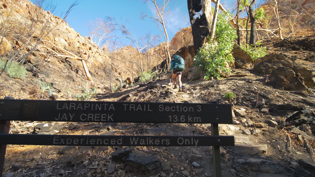 Hiker walks past sign to Jay Creek on Larapinta Trail, Central Australia
