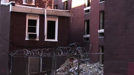 A-Cyclone-Fence-And-Barbedwire-Should-Prevent-Unwanted-Visitors-From-Accessing-An-Airconditioner-That-Still-Sits-In-A-Window-Of-An-Abandoned-Building