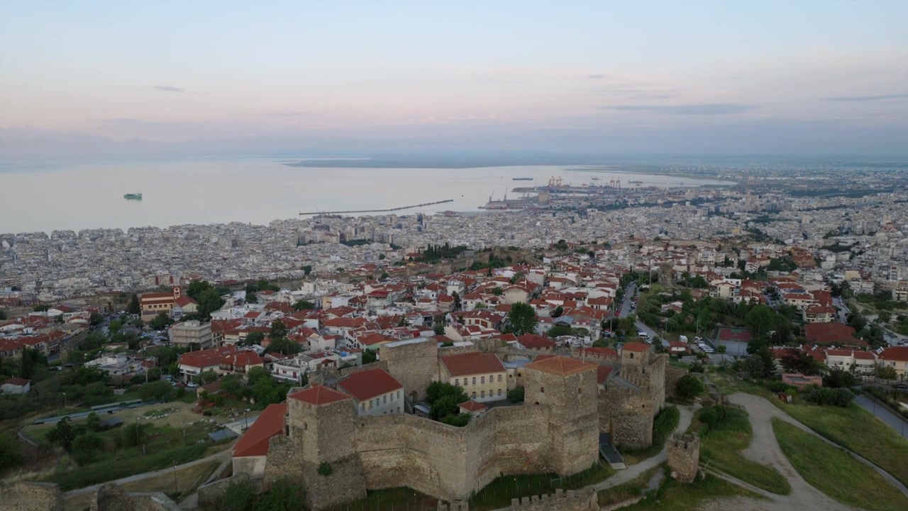 Luftfoto med drone ved solopgang af Heptapyrgion-fæstningsmurene i Thessaloniki, Grækenland, med byen og Den Thermaiske Bugt strækkende sig mod horisonten.