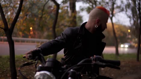 portrait of a man sitting on chopper bike between trees turns on headlight