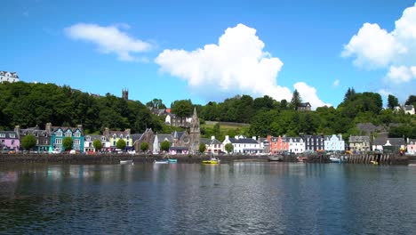 Weiße-Wolken-Bewegen-Sich-Langsam-Hinter-Dem-Hügel-Des-Hübschen-Dorfes-Tobermory,-Während-Kleine-Wellen-Im-Plätschernden-Wasser-Im-Vordergrund-Vorbeiziehen