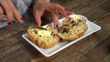 Mujer-Joven-Esparciendo-Mantequilla-En-El-Tradicional-Bollo-Casero-De-Nueva-Zelanda-En-Un-Elegante-Café