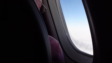 Man-looking-out-of-airplane-window-at-blue-sky-and-clouds