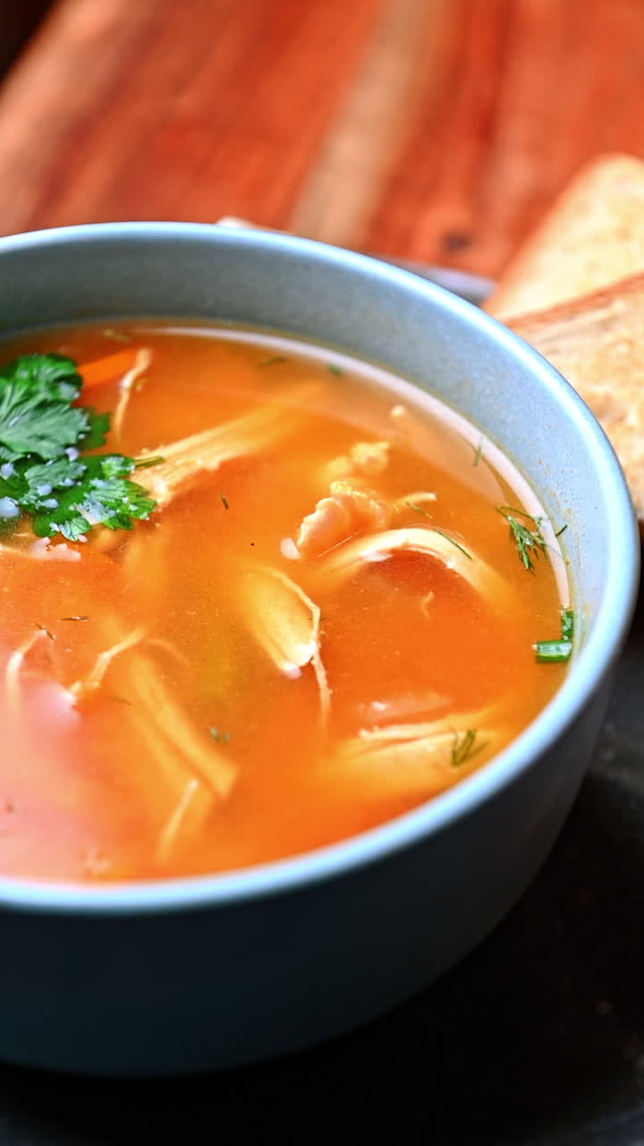 Homemade chicken soup with vegetables and herbs. Hot chicken broth with vegetables, parsley, and dill served in ceramic bowl on wooden table