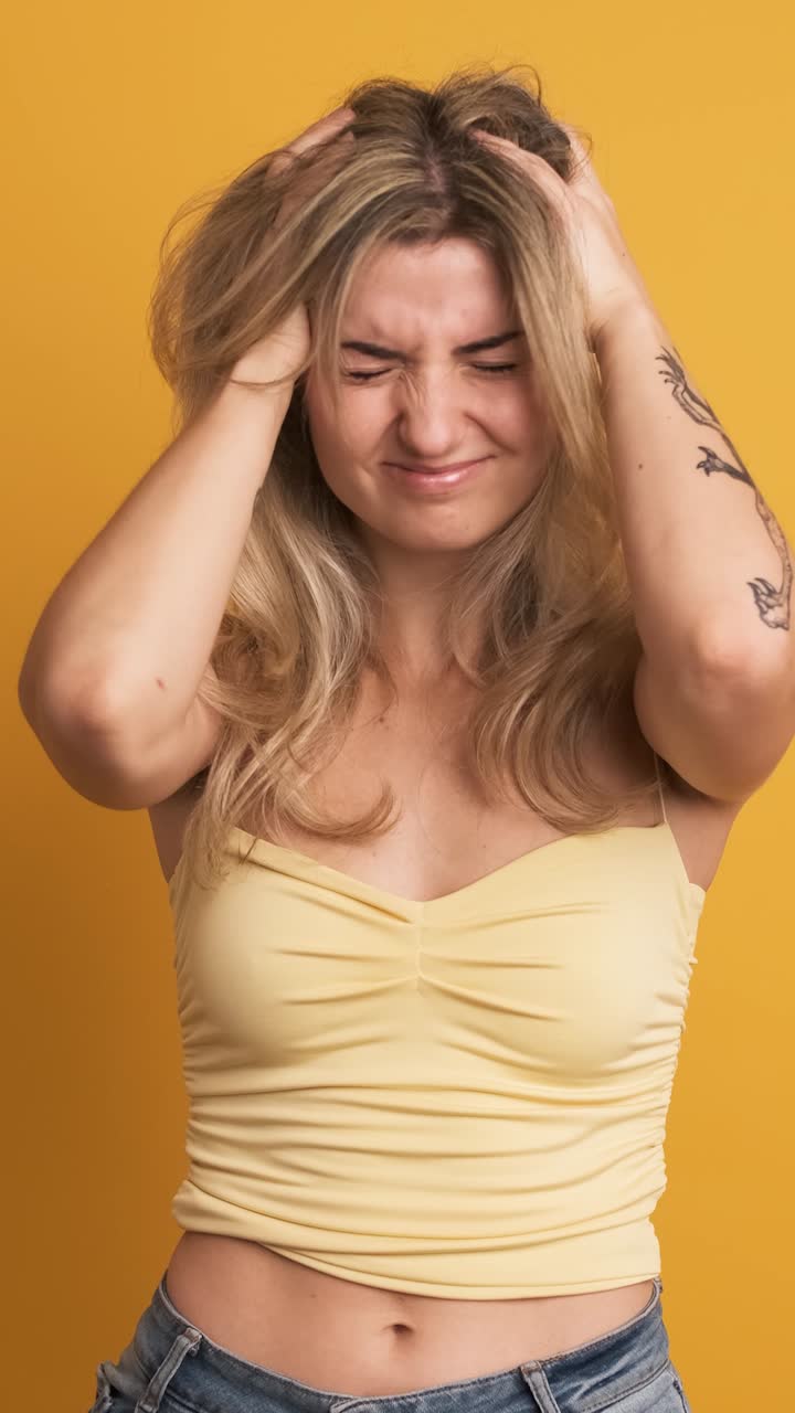 Sad young woman holding head in pain on yellow background