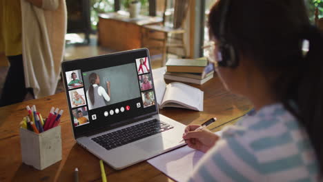 girl doing homework and having a video conference with teacher and classmates on laptop at home