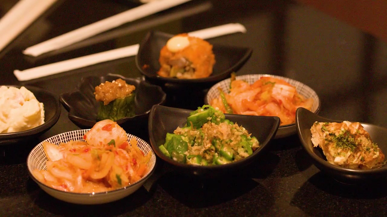 Mão colocando pequenas tigelas de acompanhamentos japoneses na mesa