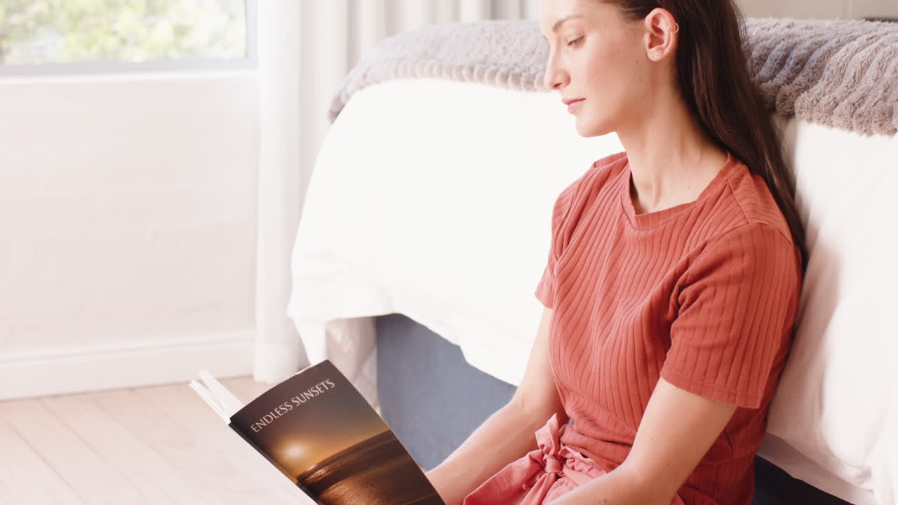 Woman sitting on floor reading book, relaxing in bright bedroom