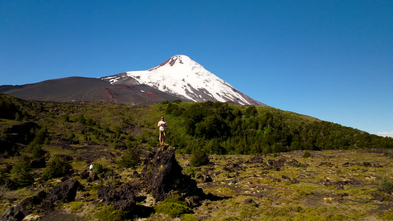 Aerial past traveler on rocky outcrop toward snow-capped Osorno volcano, Chile