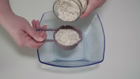 measuring rolled oats from glass jar into mixing bowl, overhead closeup