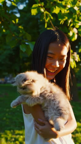 happy young woman cuddling her fluffy cat outdoors in sunlight