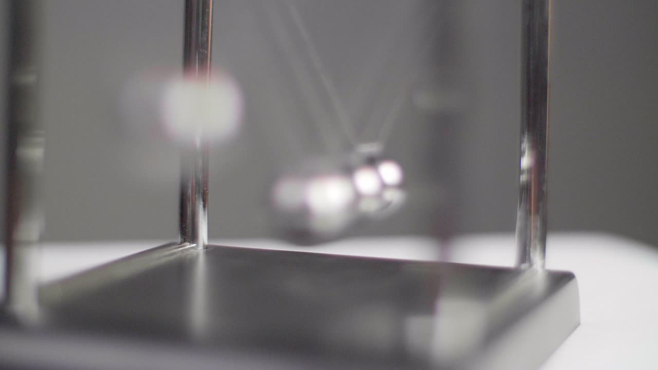 Slow motion: Newton's cradles swinging on a white minimal surface with a dark background in Slow Motion. Camera backwards movement. Shot in 4K.