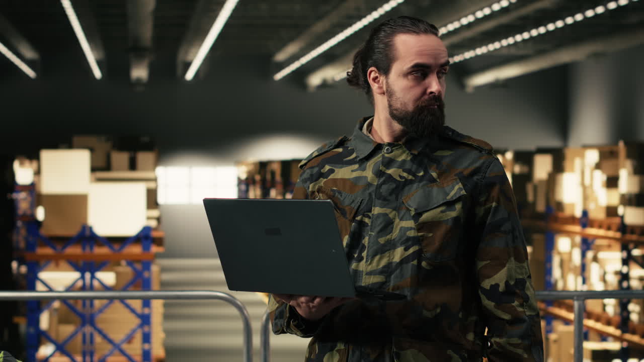 Pracownik magazynu w kurtce moro korzystający z laptopa do zarządzania zapasami