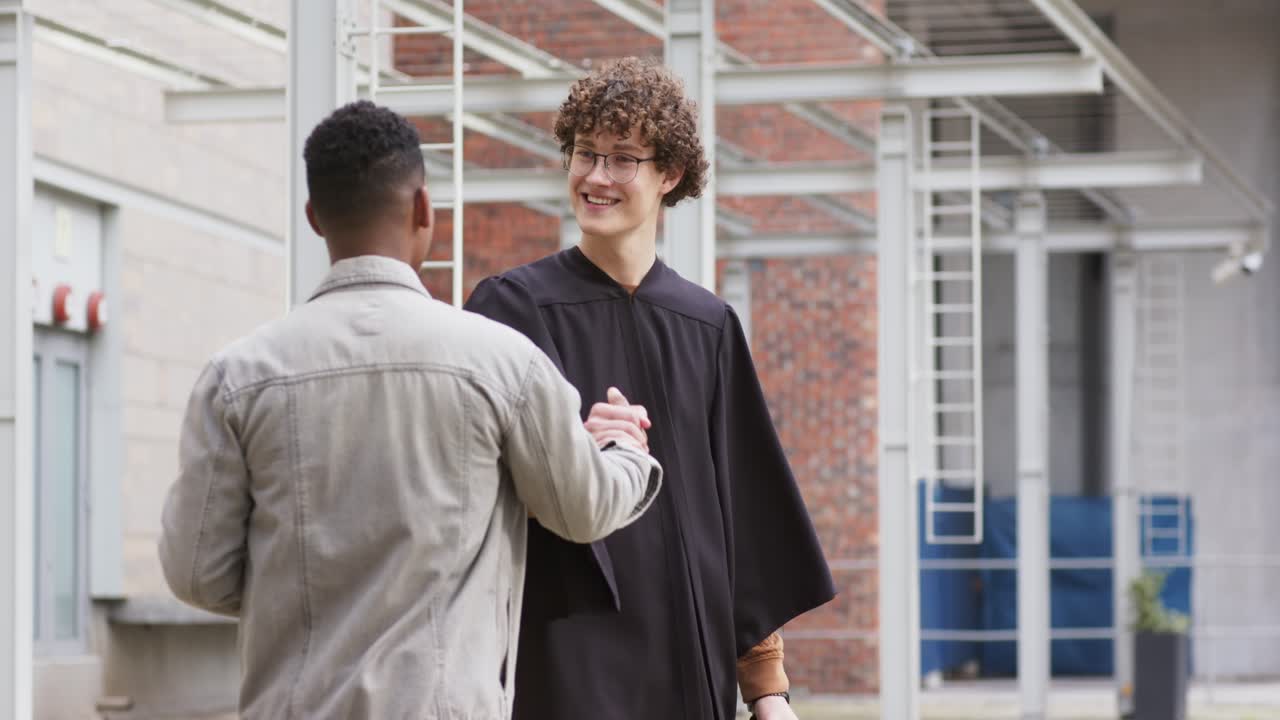 Diverse mannelijke vrienden zwaaien, omhelzen, passen hun pet aan terwijl ze een toga dragen op een binnenplaats, met koffie in de hand.