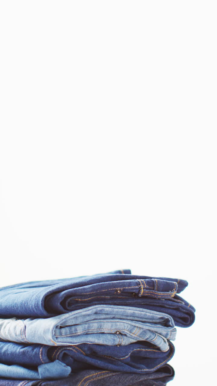 Vertical video of folded jeans with different shades on white background with copy space