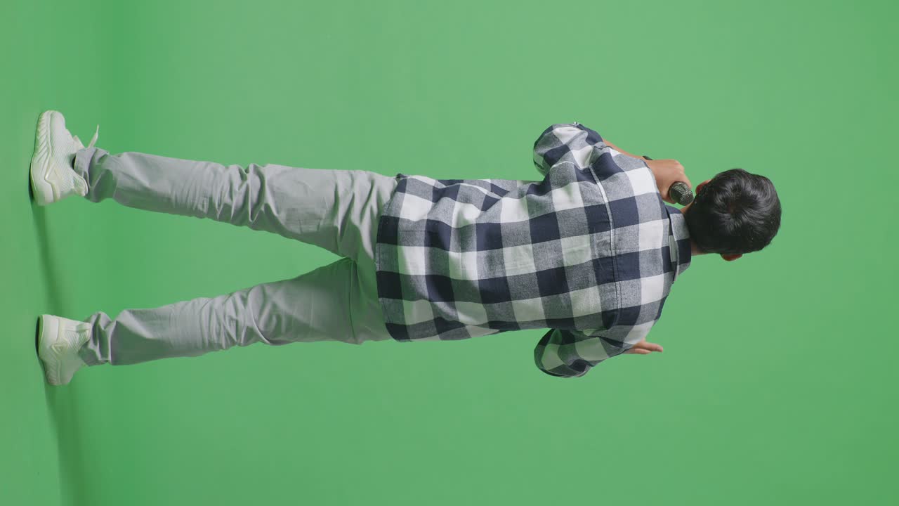 녹색 스크린 배경에서 마이크를 들고 노래하는 젊은 아시아 십대 소년의 전체 몸의 뒷면