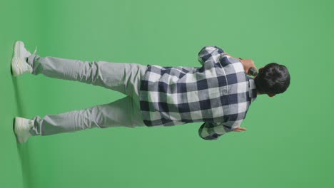 녹색 스크린 배경에서 마이크를 들고 노래하는 젊은 아시아 십대 소년의 전체 몸의 뒷면