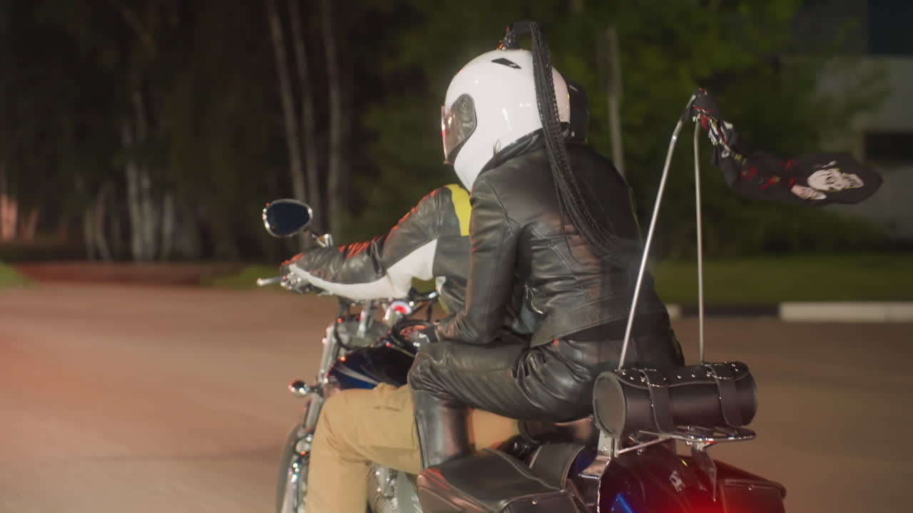 Rear view of motorcyclists riding at normal speed on evening road, leather jackets and helmets visible as scarf tied to bike flutters in wind, capturing motion and freedom of night journey