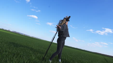 Young attractive long-haired girl dancing actively and holding a microphone stand. Lady posing in front of camera shooting rock music video at nature backdrop.
