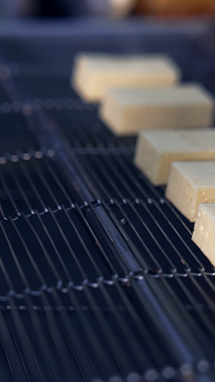 Hands in blue gloves lay out soft milky bars at the conveyor grid. Manufacturing of sweet desserts at the confectionery plant. Vertical video