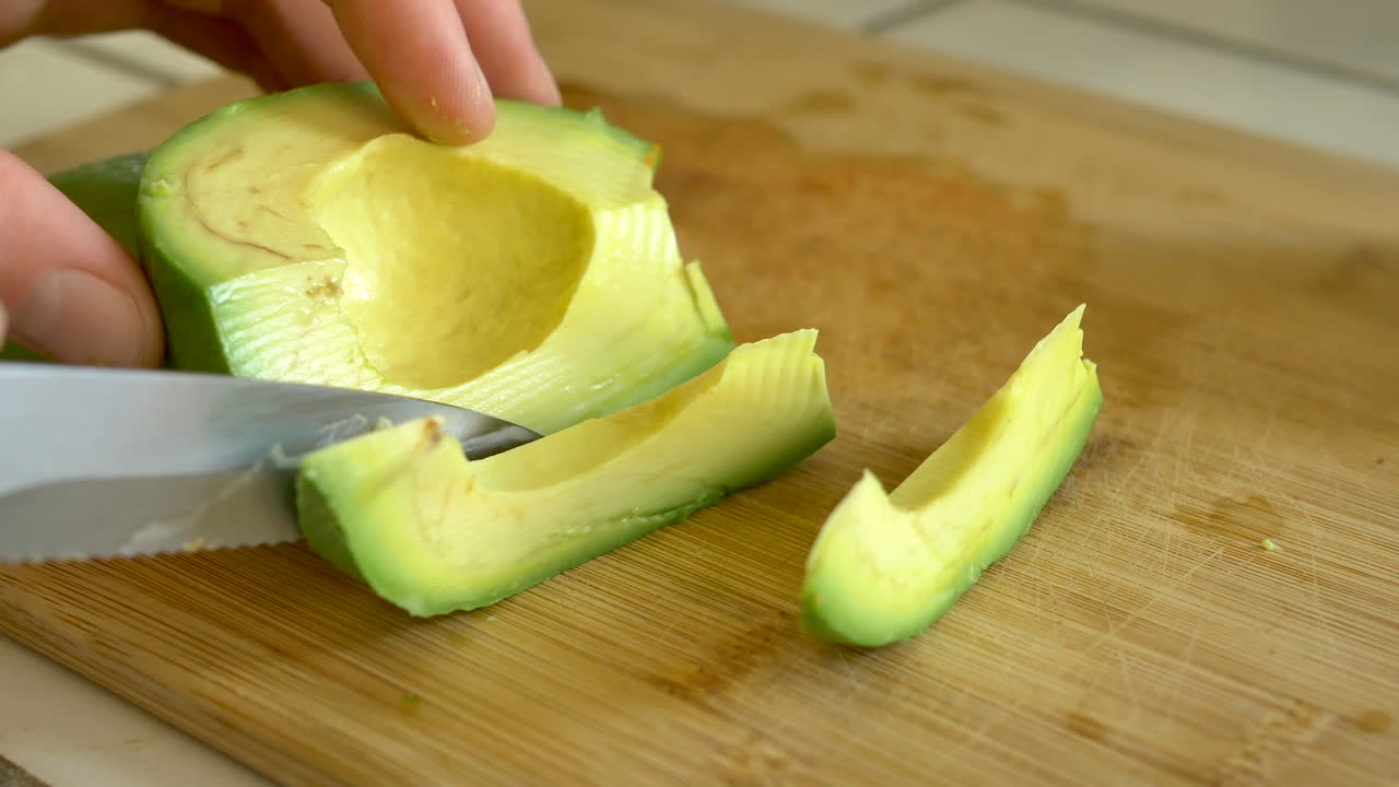 Uno chef taglia un avocado verde maturo su un tagliere di bambù mentre prepara un sano pranzo vegano in cucina