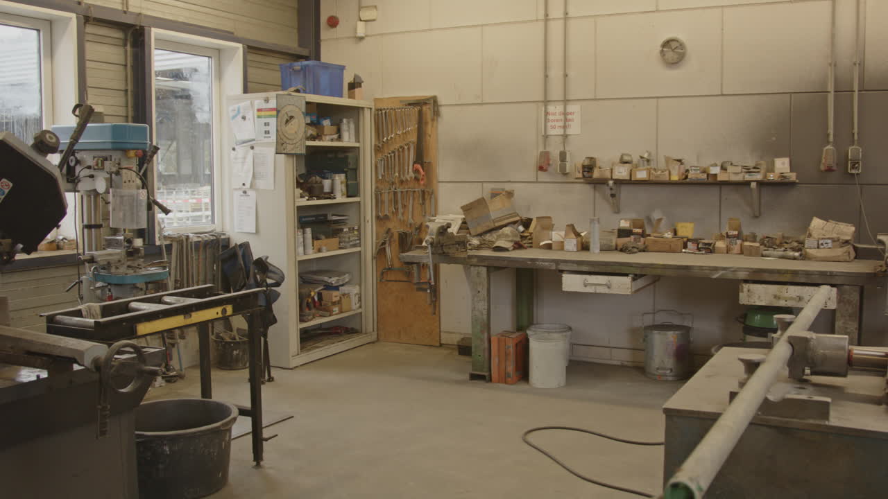 Pan of a large and tidy metal workshop inside a factory. Several workbenches, storage closets and equipment are in the room