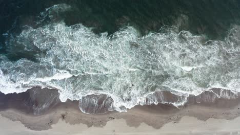 aerial view of ocean waves crashing on sandy beach