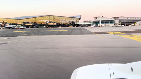 View-from-an-airplane-window-on-the-tarmac,-sunrise-at-the-airport,-aircraft-wing-in-the-foreground