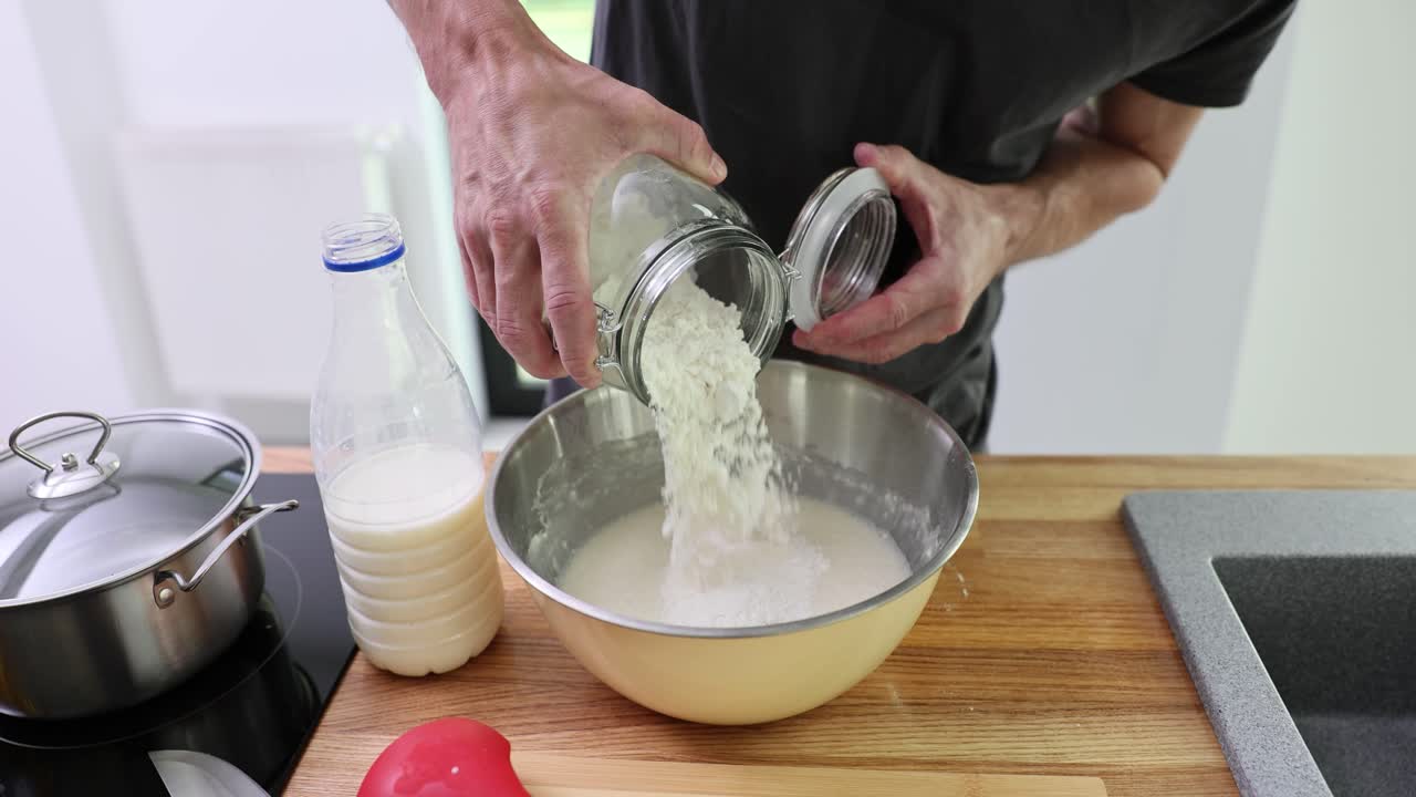 Mani d'uomo versano farina di grano in una ciotola con latte su un bancone di legno