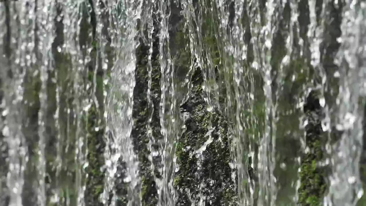 A detailed shot captures streams of clean water rushing over mossy rocks of a waterfall.