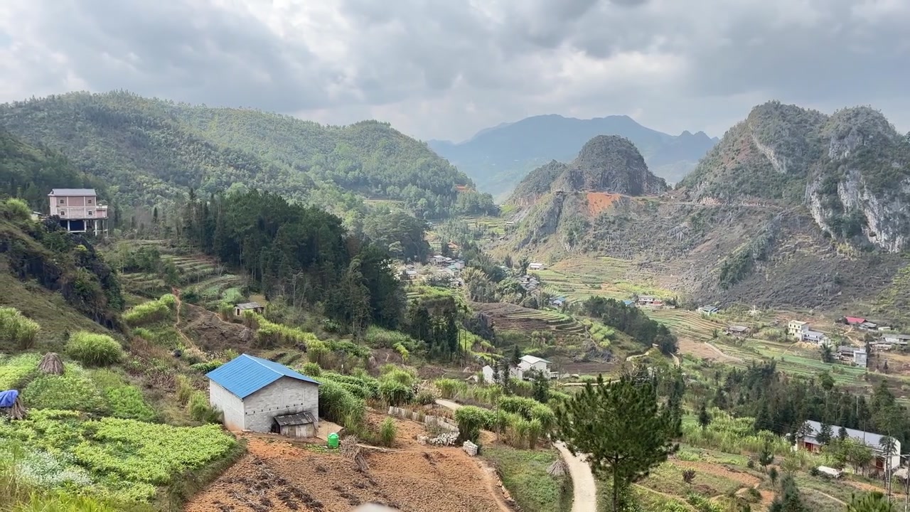 Pemandangan lanskap luas desa kecil dengan atap biru dan sawah terasering di Jalur Ma Pi Leng, Ha Giang, Vietnam, dikelilingi oleh pegunungan karst kapur.
