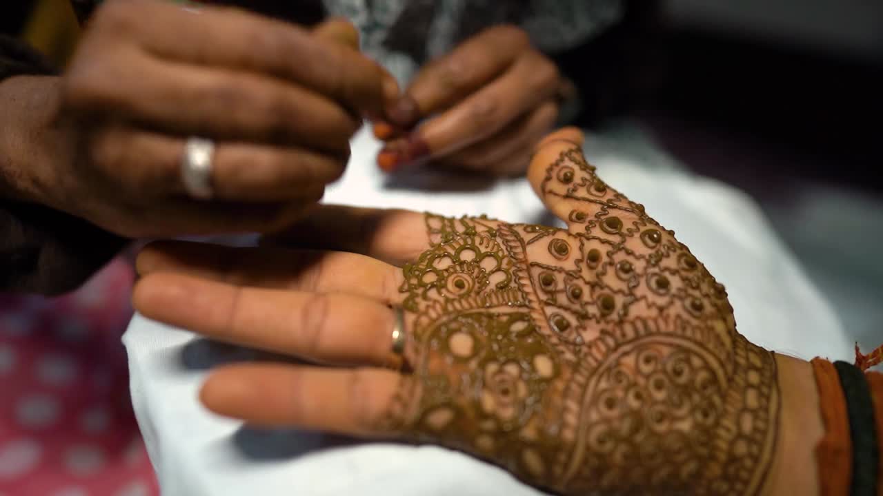 Un artista di mehndi che realizza intricati design con l'henné sulla mano dello sposo durante una tradizionale cerimonia nuziale indiana