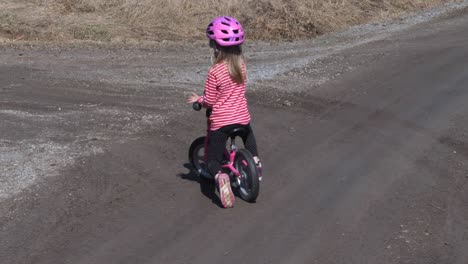 handheld, slow motion shot of a little girl cycling on a gravel road, on the finnish countryside, on a sunny spring day, in vaasa, ostrobothnia, finland