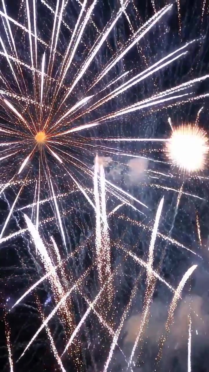 Vertikales Video: Aufsteigende Raketen erzeugen Explosionen und kreuzende Streifen am Nachthimmel, Hochformat-Aufnahme.