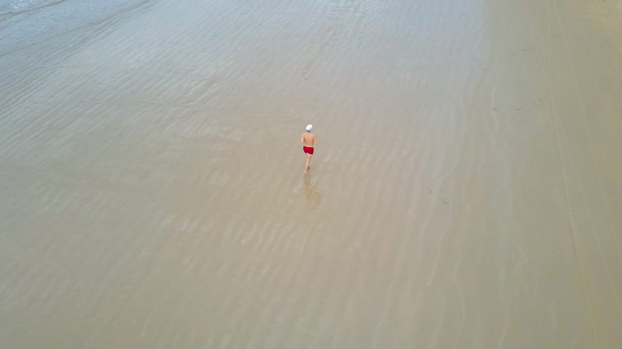 푸른 물이 있는 완벽한 해변을 달리는 남자의 드론 보기