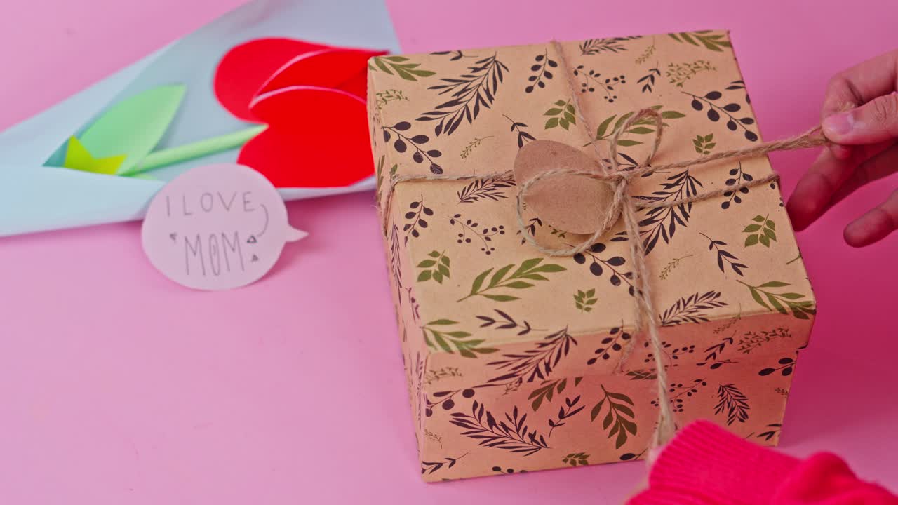 Woman's hands carefully pulling twine on decorated gift box for Mother's Day celebration