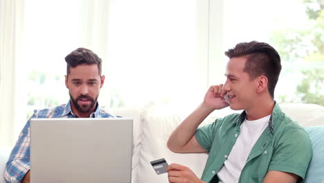 pareja gay relajándose en el sofá usando una computadora portátil