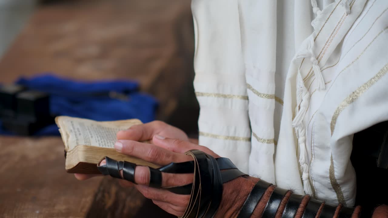 Close-up de mãos virando as páginas de um livro de orações com tefilin e talit