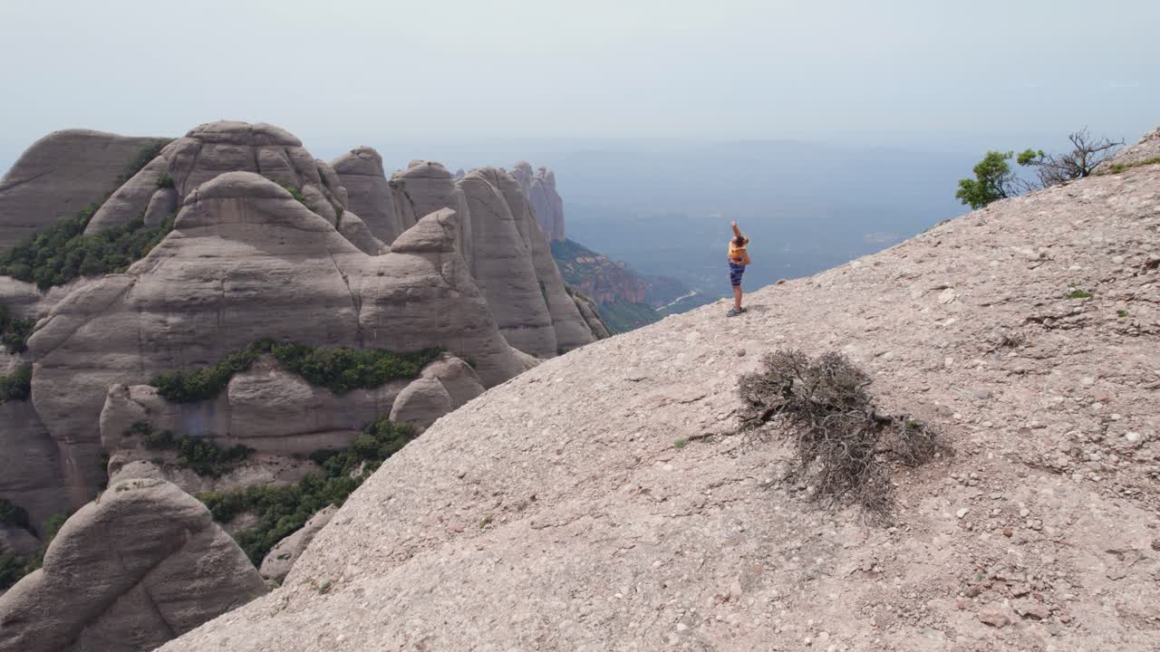 mujer joven estirándose en medio de la naturaleza, monasterio de montserrat, barcelona, toma cinematográfica de drones, concepto de bienestar y salud