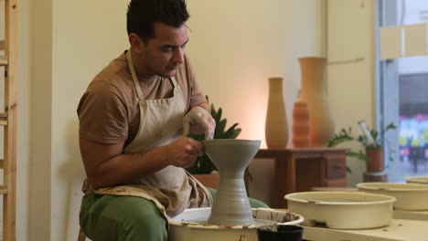 Artesano-Masculino-En-Cámara-Lenta-Formando-Una-Escultura-De-Jarrón-De-Arcilla-En-Un-Torno-De-Alfarería-De-Taller