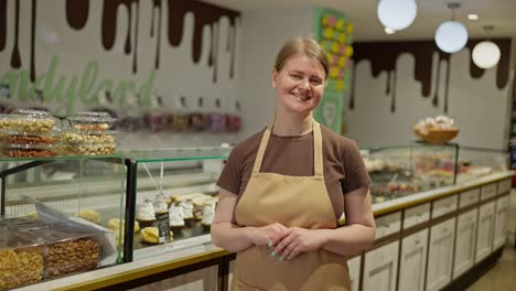 Porträt-Eines-Glücklichen-Mädchens-In-Einem-Braunen-T-Shirt-Und-Einer-Schürze,-Das-In-Der-Nähe-Einer-Konditorei-In-Einem-Supermarkt-Posiert.-Porträt-Eines-Glücklichen-Mädchens,-Das-Während-Seiner-Arbeitsschicht-In-Einer-Konditorei-In-Einem-Supermarkt-Arbeitet