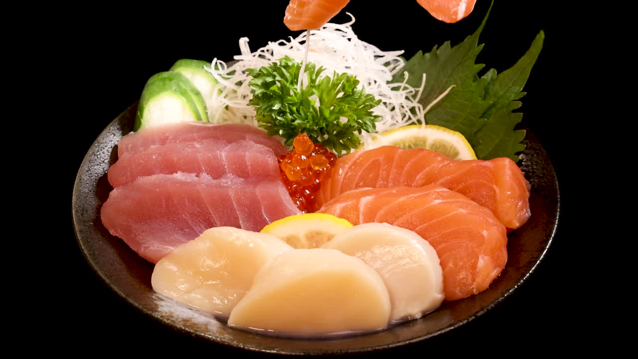 Chopsticks lift a slice of salmon sashimi from a vibrant assorted sashimi and sushi set, under bright studio lighting with a black background