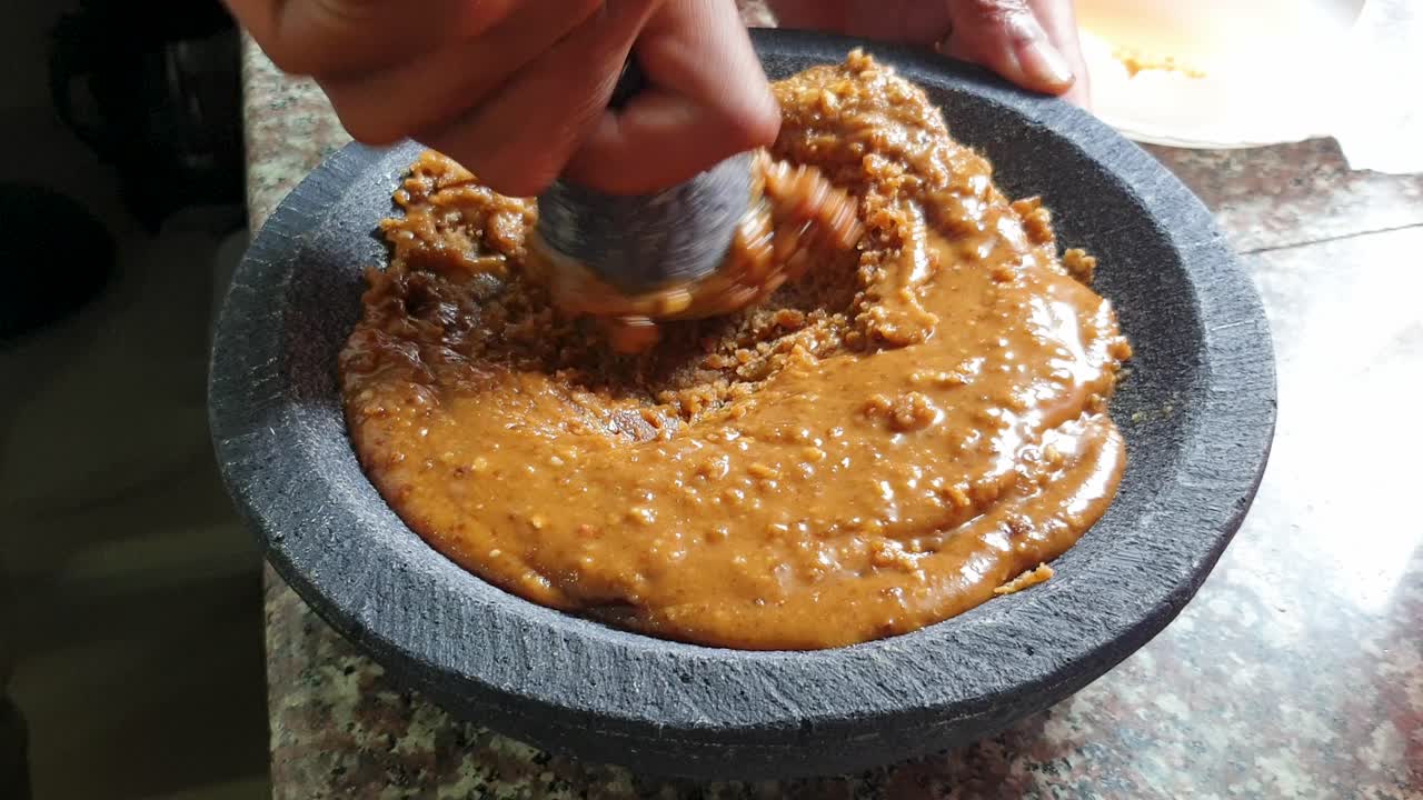 Palm sugar and ingredients being mashed into sweet sticky syrup with mortar and pestle, close up of food preparation action